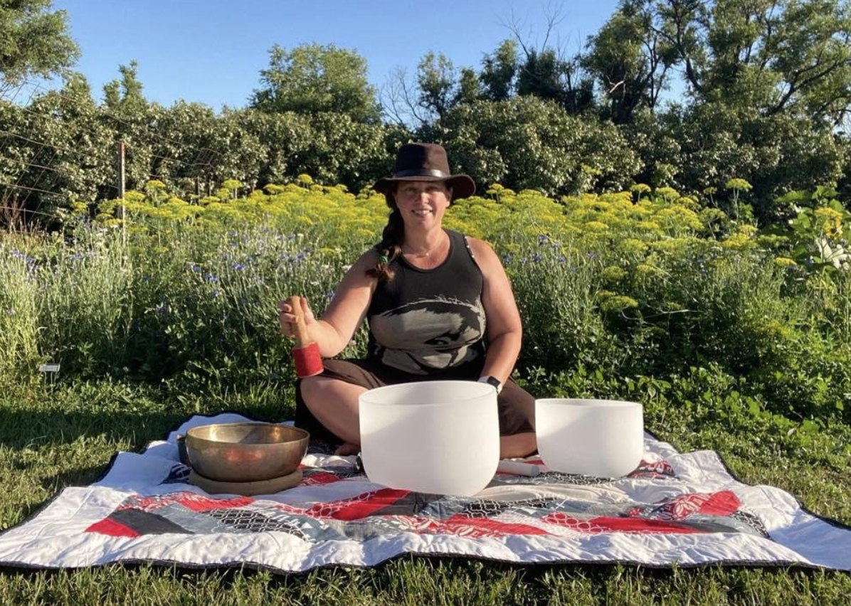 a woman playing crystal bowls in a garden setting