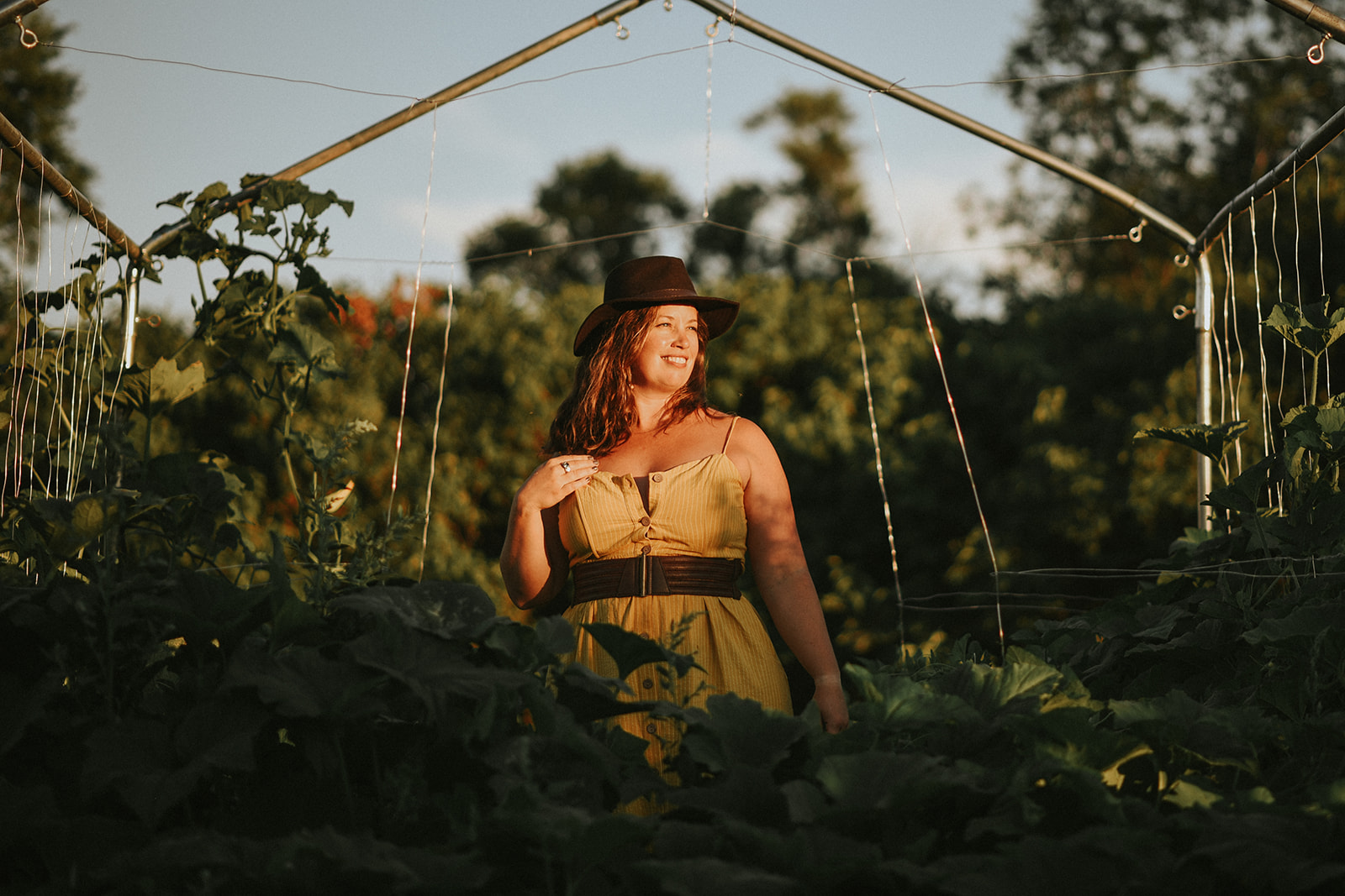 a woman stands in her garden in the waning sunlight